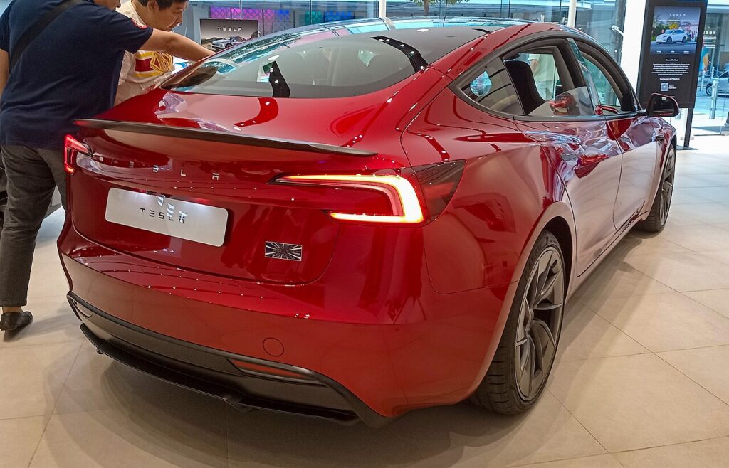 Red Tesla Model 3 rear quarter and painted bumper under showroom lighting