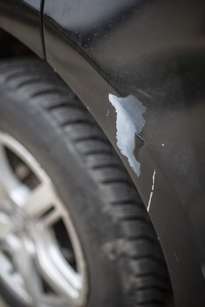 Missing and peeling paint beside a black car wheel arch