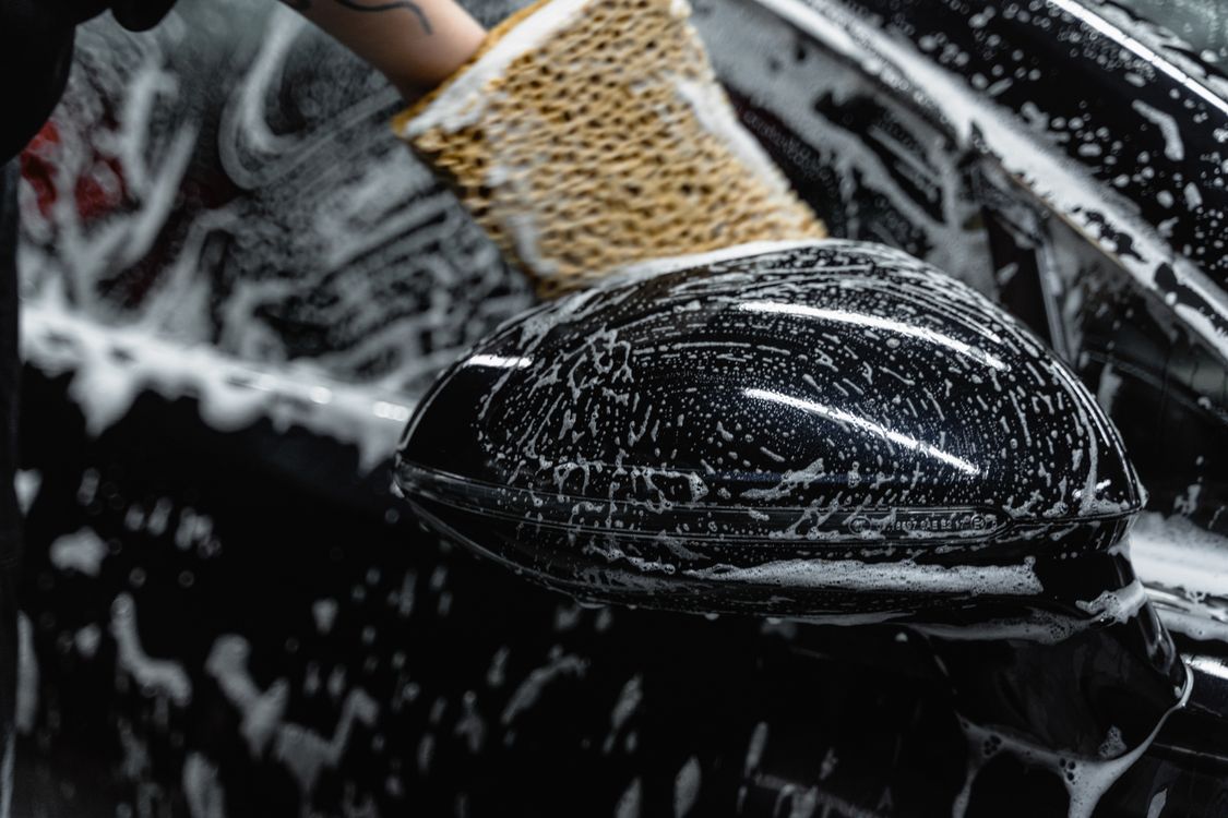 A hand washing a soapy car mirror