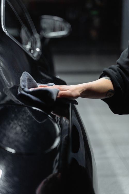 A hand wiping a dark car panel with a microfiber cloth