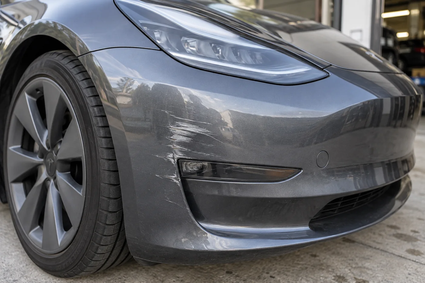 Scuffed front bumper beside the headlamp of a grey Tesla