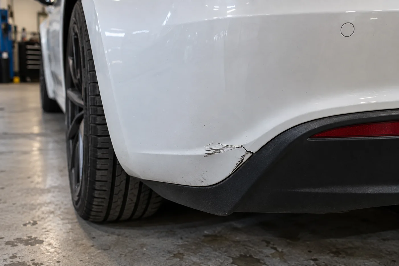Short crack and scrape near the lower corner of a white Tesla bumper