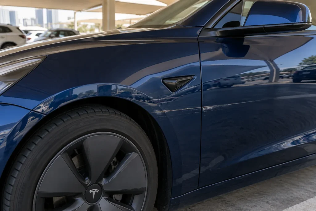 Horizontal scrape across the blue paint of a Tesla door and front fender